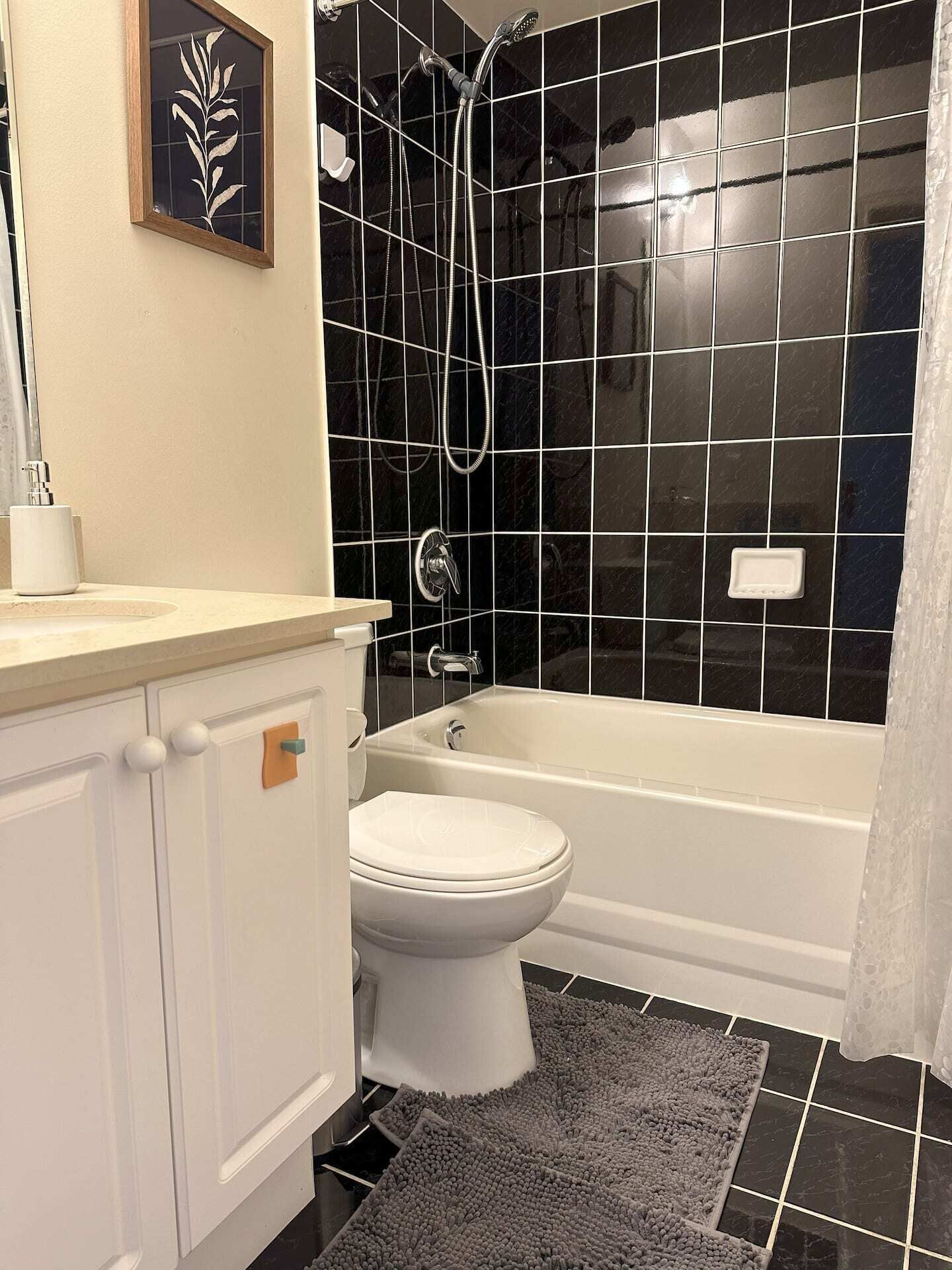 A bathroom with a white toilet, a bathtub, and a shower area with black tiles.