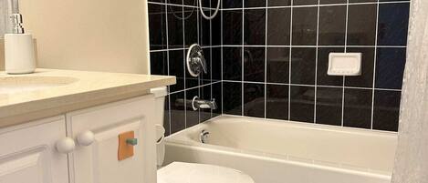A bathroom with a white toilet, a bathtub, and a shower area with black tiles.