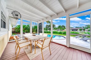 A covered patio with a pool, wooden deck, and a table with chairs. - Waterfront, Hot Pool, Lounge Patio, Beach House (Palm Beach Gardens)