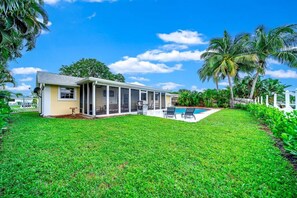 A house with a covered patio, a swimming pool, and lush greenery. - Waterfront, Hot Pool, Lounge Patio, Beach House (Palm Beach Gardens)