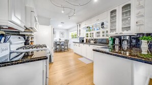 Une cuisine moderne avec des meubles blancs, un plan de travail en granit et un coin repas comprenant une table et des chaises.