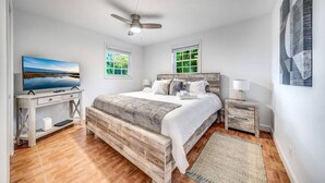 Une chambre à coucher avec un lit en bois, un bureau, une télévision et un ventilateur de plafond.