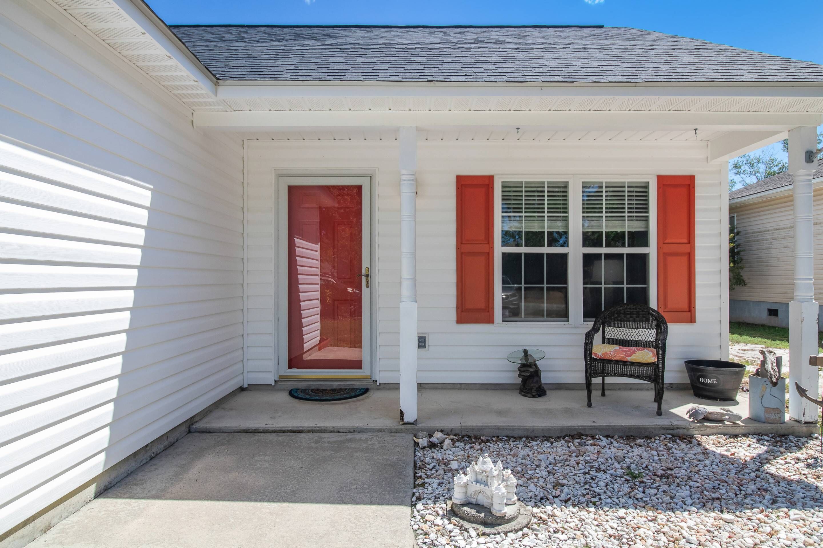 A white house with red shutters, a front porch, and a small garden area.