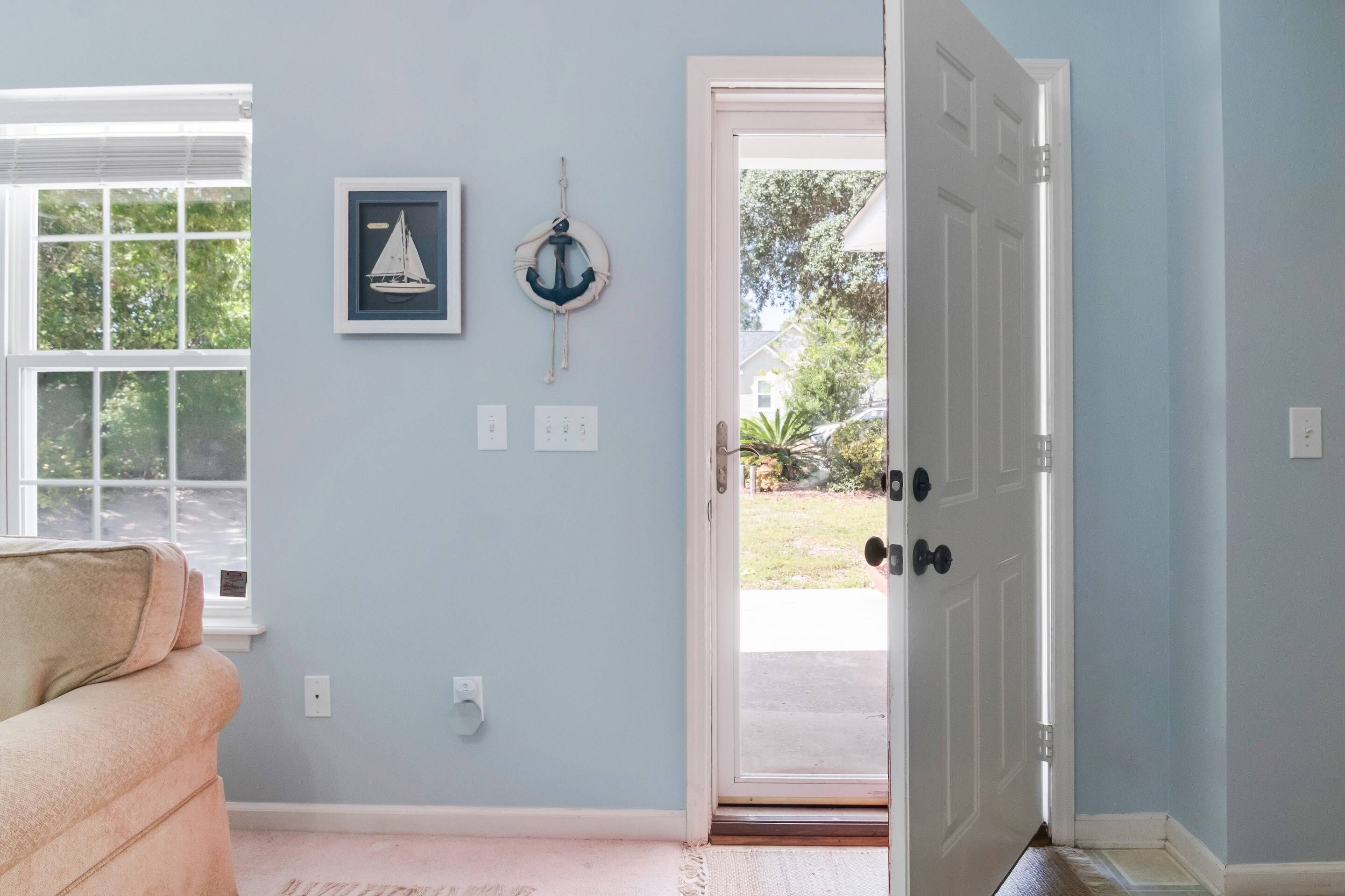 Ein Zimmer mit hellblauer Wand, einem gerahmten Bild von einem Segelboot, einem Rettungsflossensymbol und einem beigen Sofa.
