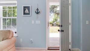 A room with a light blue wall, a framed sailboat picture, a life preserver, and a beige couch. - Charming Home! Just minutes From the Beach, Near Shopping, Dog Friendly (Oak Island)