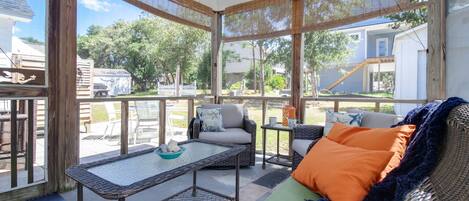 Un patio techado con mobiliario de mimbre, una mesa de vidrio y vistas al jardín trasero.
