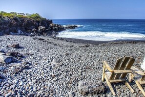 A rocky beach with a wooden chair and a white structure in the background.