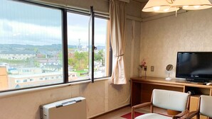 A hotel room with a large window, a TV, a desk, and a chair.