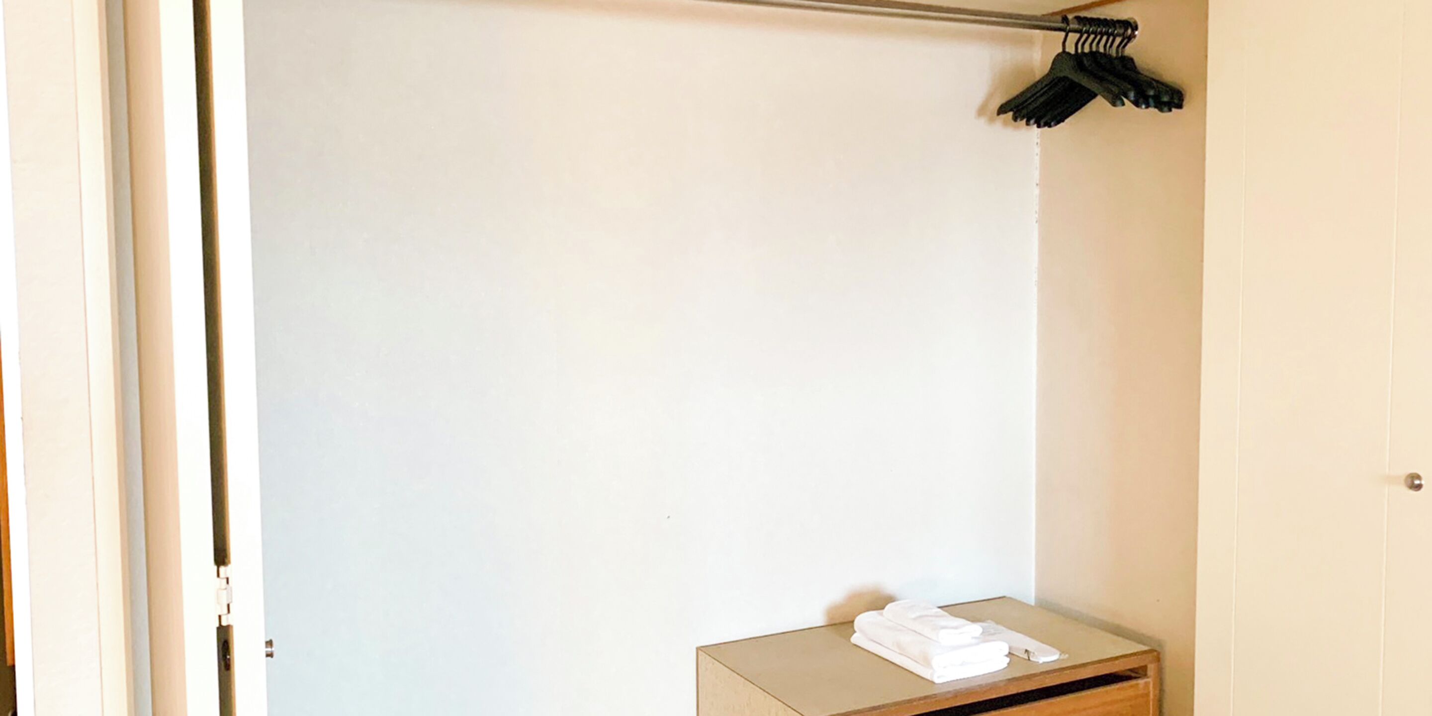 A hotel room with a large closet, a small wooden table with folded towels, and a coat rack with hanging items.