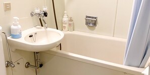 A bathroom with a white sink, a bathtub, and a shower. There are toiletries on the sink and a towel rack on the wall.
