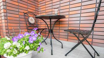 A small outdoor seating area with a metal table and chairs, a potted plant with flowers, and a decorative tile wall.