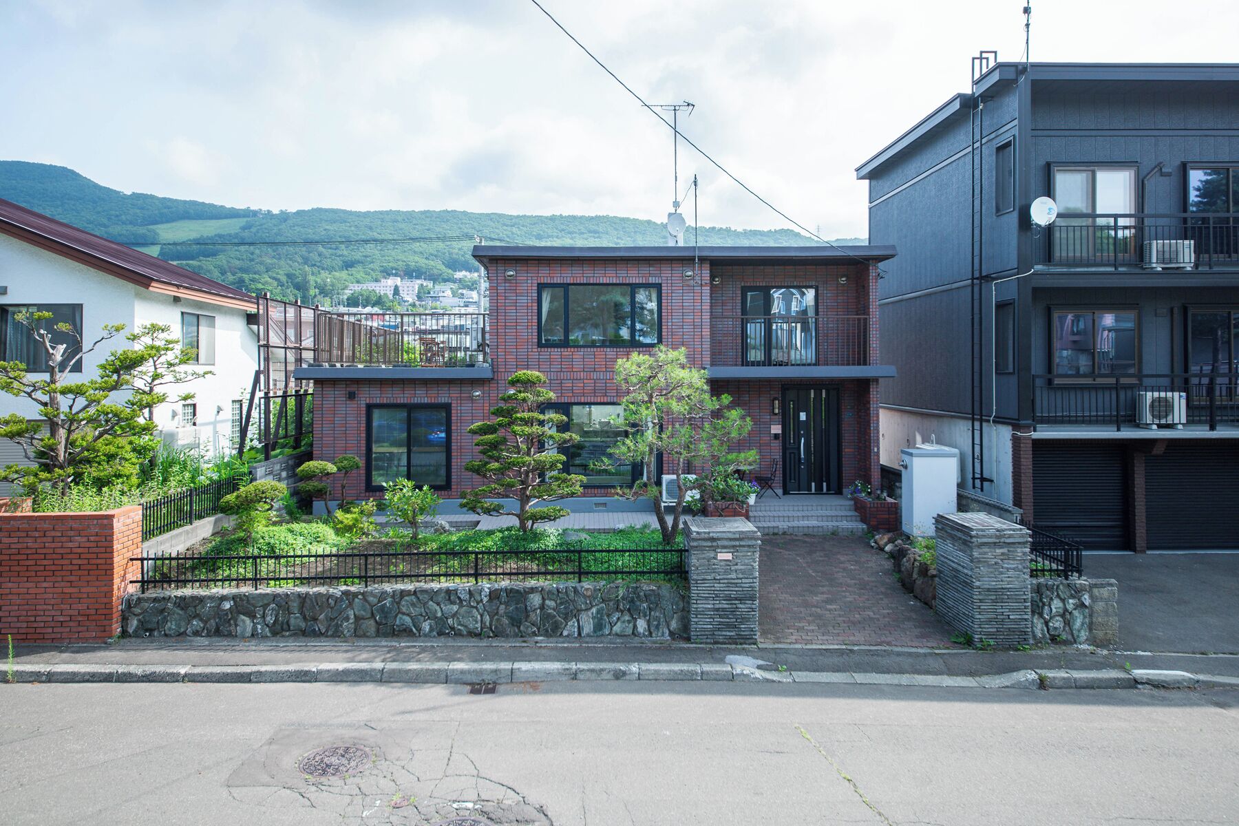 A modern residential building with a stone facade, a balcony, and a view of a hilly landscape.