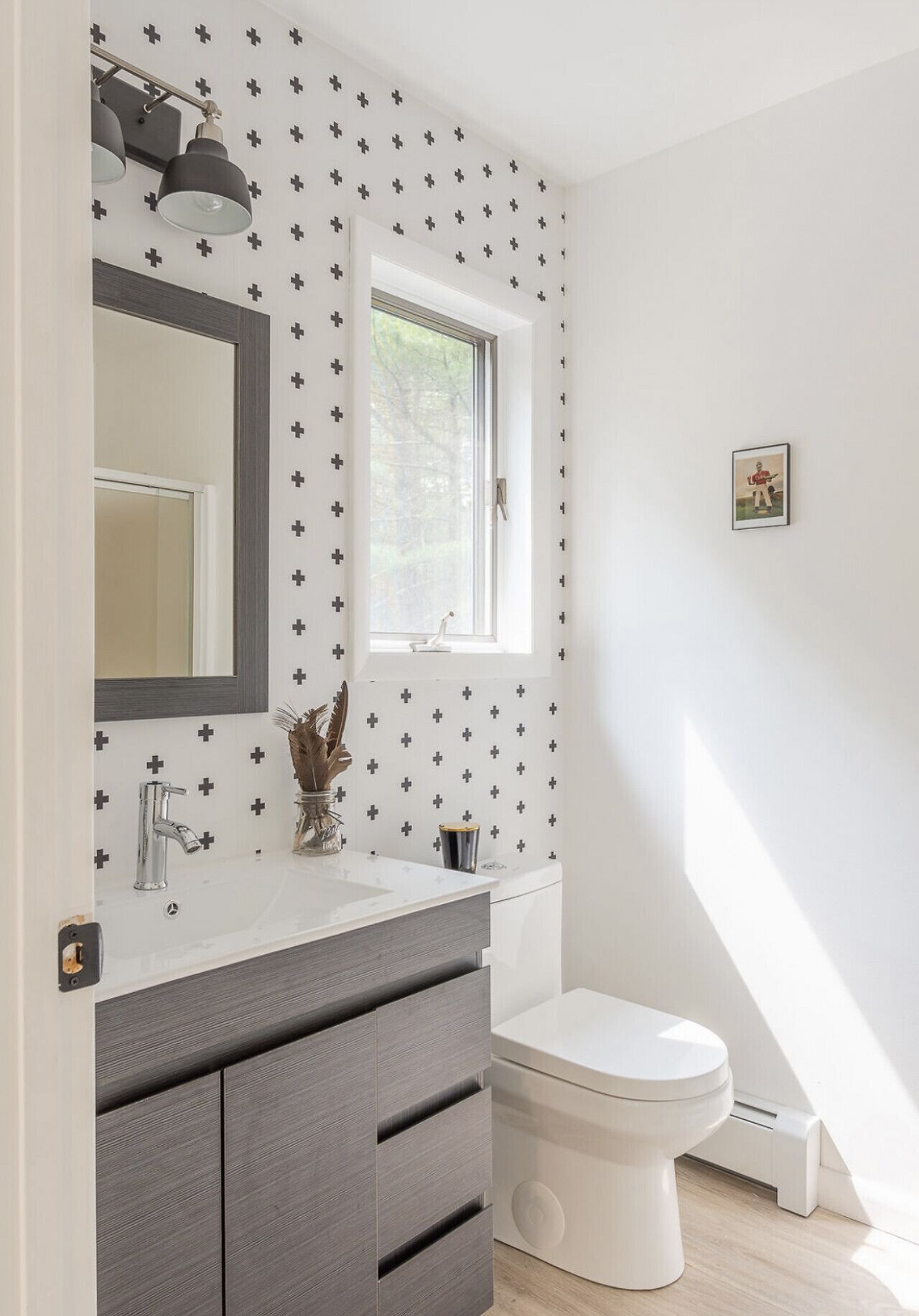 Een badkamer met een witte wastafel, een donkergrijze kast, een wit toilet en een raam met uitzicht op bomen.