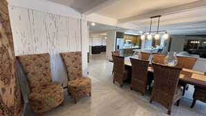 Un espace repas avec une grande table et des chaises, une cuisine à l’arrière-plan et un salon avec des canapés.