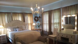 A bedroom with a large bed, a sitting area, a vanity with a mirror, and a chandelier.