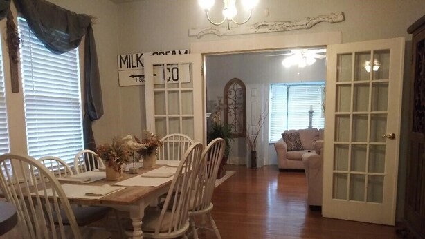 A dining area with a wooden table and white chairs, a white door with glass panels, and a sign on the wall reading "MILK COFFEE".