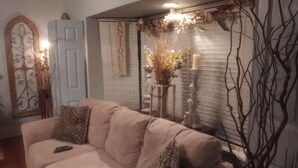 A living room with a beige sofa, decorative wall art, a white door, and a window with blinds.