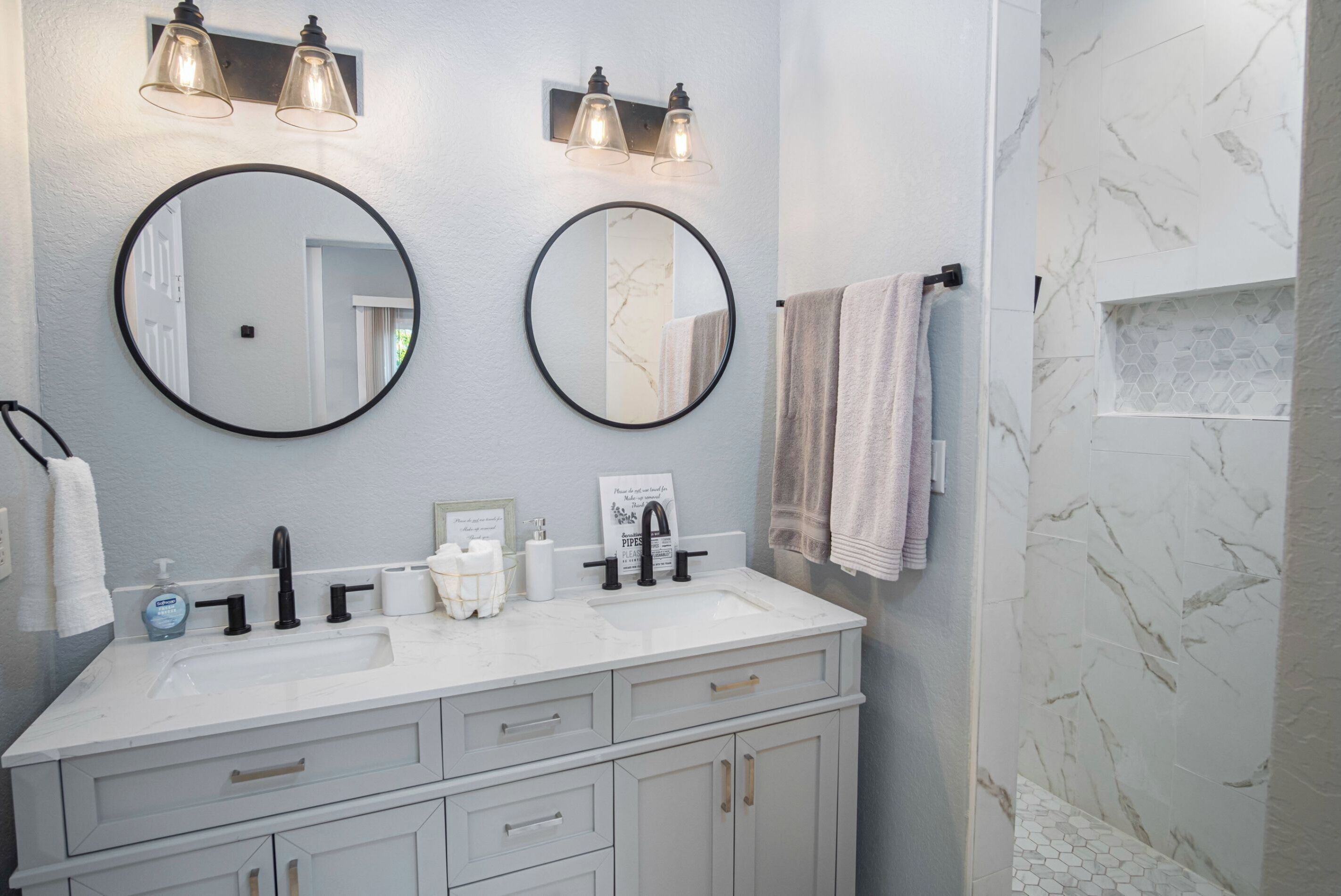 Un baño con dos espejos redondos, un lavabo blanco y un perchero para toallas.