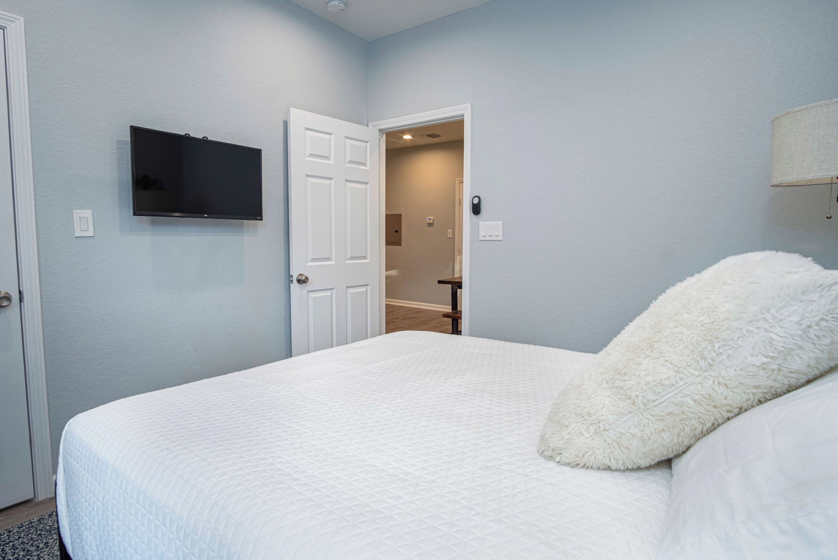 Une chambre à coucher avec un lit, un téléviseur fixé au mur et une porte donnant sur une salle de bain.