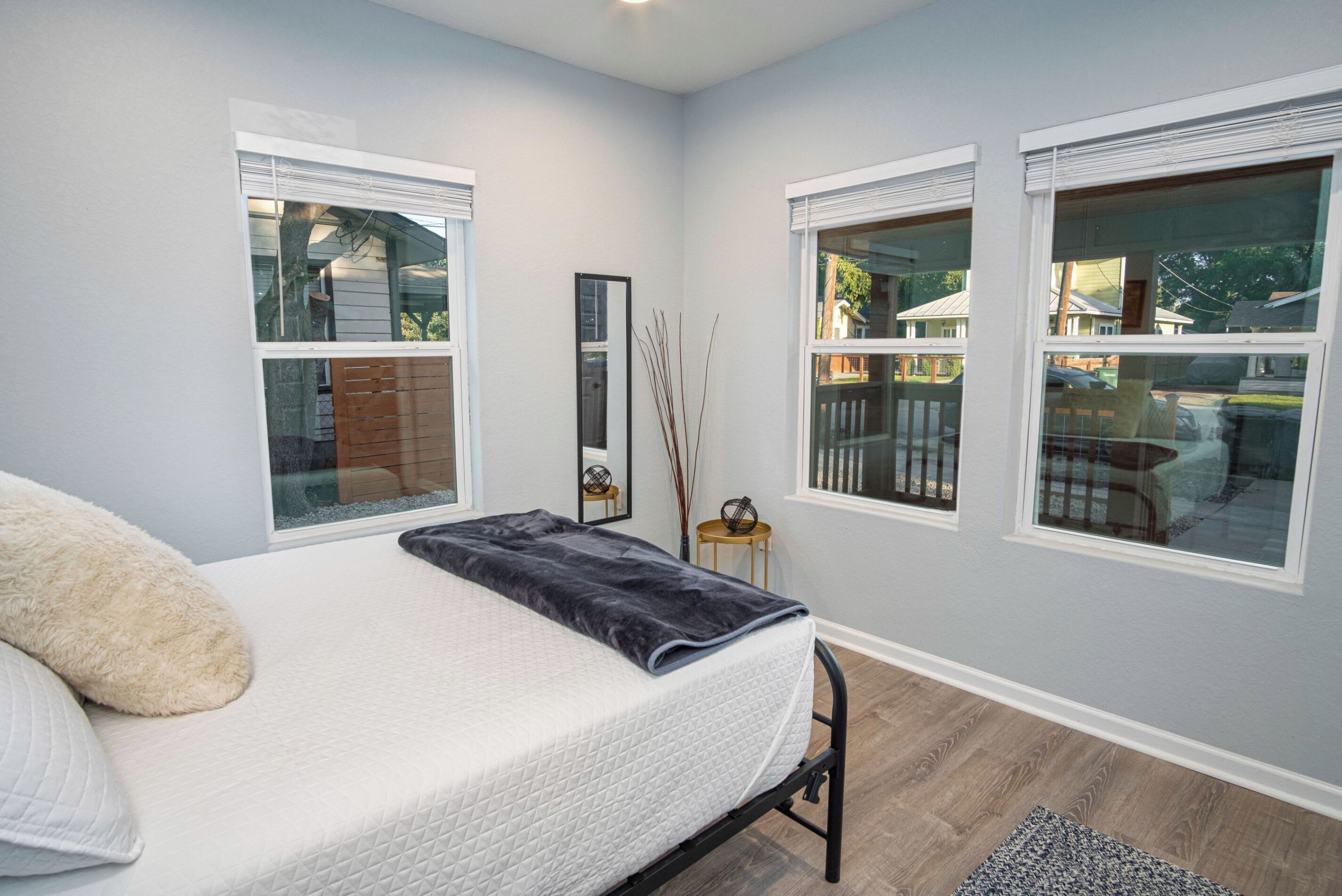 A bedroom with a bed, two windows, a mirror, and a small side table.