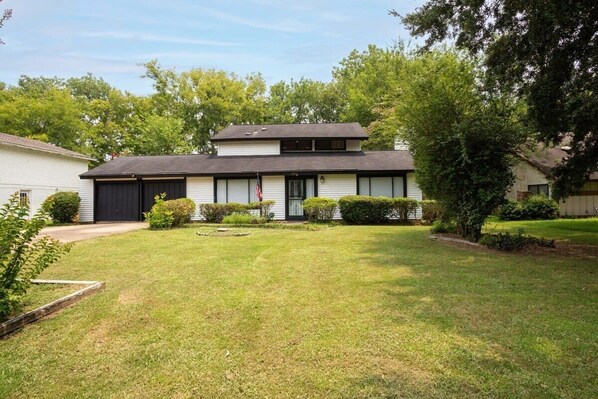 A two-story house with a front garage, a well-maintained lawn, and a large tree to the right.