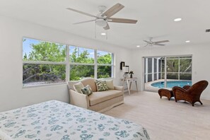 A spacious room with a large bed, a sofa, a chair, and a view of a swimming pool.