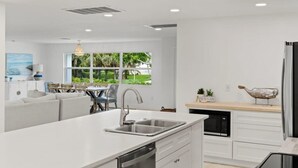 Une cuisine moderne dotée d’un îlot central, de meubles blancs et offrant une vue sur la verdure environnante.