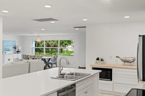 A modern kitchen with a central island, white cabinetry, and a view of greenery outside.