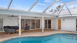 Un espace piscine doté d’un toit en verre, d’un canapé, d’un fauteuil et d’une petite table.