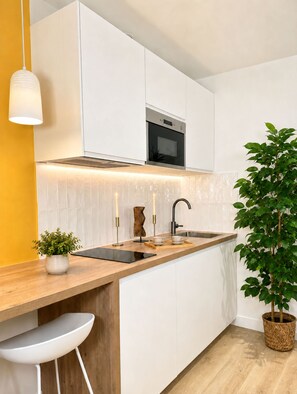 A modern kitchen with white cabinetry, a wooden countertop, a built-in oven, and a potted plant. - Charming studio - Opéra Garnier (Paris)