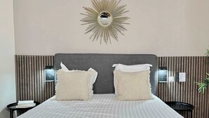 Une chambre d’hôtel avec un grand lit, deux oreillers, un miroir fixé au mur, des tables de chevet et un panneau de commande fixé au mur.
