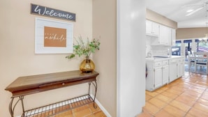 A hallway with a welcome sign, a framed sign saying "STAY awhile", and a vase with plants.