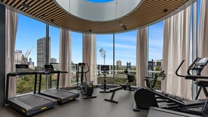 Un gimnasio moderno con cintas de correr, elípticas y una bicicleta estática, con amplias ventanas que ofrecen vistas a la ciudad.