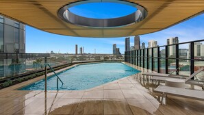 Una piscina en la azotea con barandilla de cristal, tragaluz circular y vistas panorámicas de la ciudad.