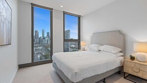 Un dormitorio moderno con una cama grande, dos ventanas con vistas a la ciudad, una mesita de noche con lámpara y un diseño minimalista.