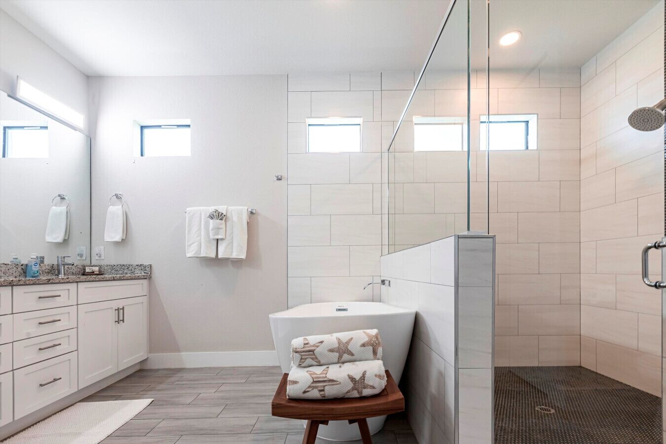 Un baño moderno con ducha, lavabo y tocador. Hay toallas colgadas en la pared y un pequeño taburete con toallas estampadas de estrellas.