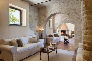 A spacious living room with a brick wall, a fireplace, and two white sofas. - Villa Verde Luna: A characteristic and welcoming two-story age-old farm house surrounded by the greenery, with Free WI-FI. (Assisi)