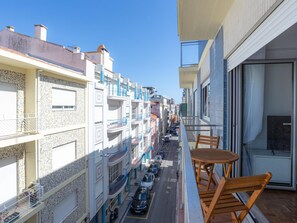 Ein Balkon mit Holztisch und -stühlen, der auf eine Straße mit parkenden Autos und Häusern mit Balkonen blickt.