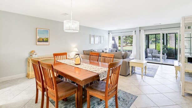 A dining area with a wooden table and chairs, a chandelier, and a sofa in the background.