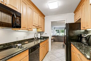 Una cocina con armarios de madera, microondas, refrigerador, lavavajillas y encimera de granito.