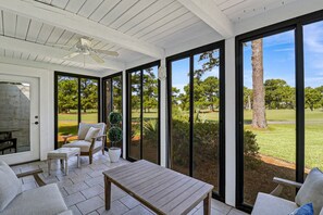 Una habitación iluminada por el sol con un amplio ventanal, un ventilador de techo y vistas a un campo de golf.