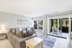 Una sala de estar con un sofá gris, una mesita y vista a un jardín a través de puertas corredizas de vidrio.