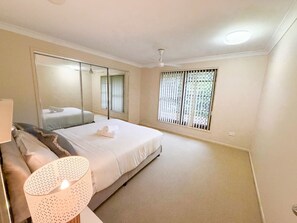 Ein Schlafzimmer mit einem Bett, einer Nachttischlampe, einem Fenster mit Jalousien und einem Deckenventilator.
