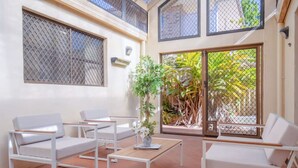 A spacious patio with white furniture, including sofas and a table, and a large sliding glass door leading to a garden.