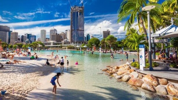 A beach with clear water, palm trees, and a city skyline in the background.