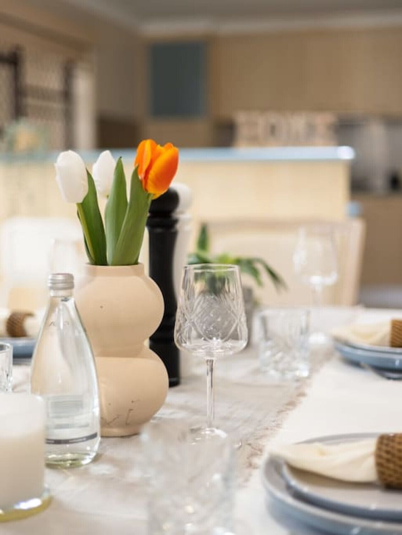 A dining table set with a vase of tulips, a glass bottle, and a wine glass.