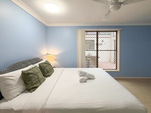 A bedroom with a bed, pillows, a nightstand with a lamp, a window with a view, and a ceiling fan.