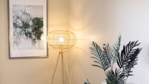 A room with a bed, a floor lamp, a framed artwork, and a potted plant.
