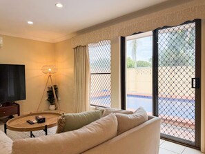 A living room with a sofa, a coffee table, a TV, and a view of a pool through a glass door.