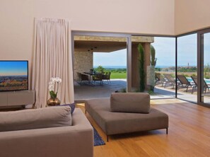 Relax in this spacious living room with a large flat-screen TV and a view of the outdoor patio area featuring a pool and lounge chairs.